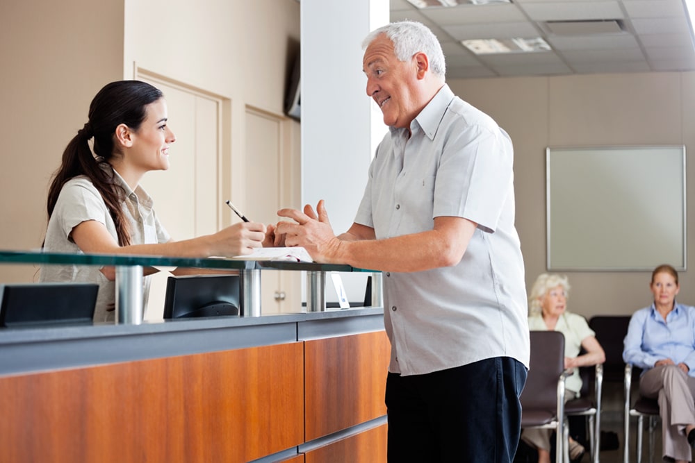 Dental practice receptionist assisting an older male patient at the front desk